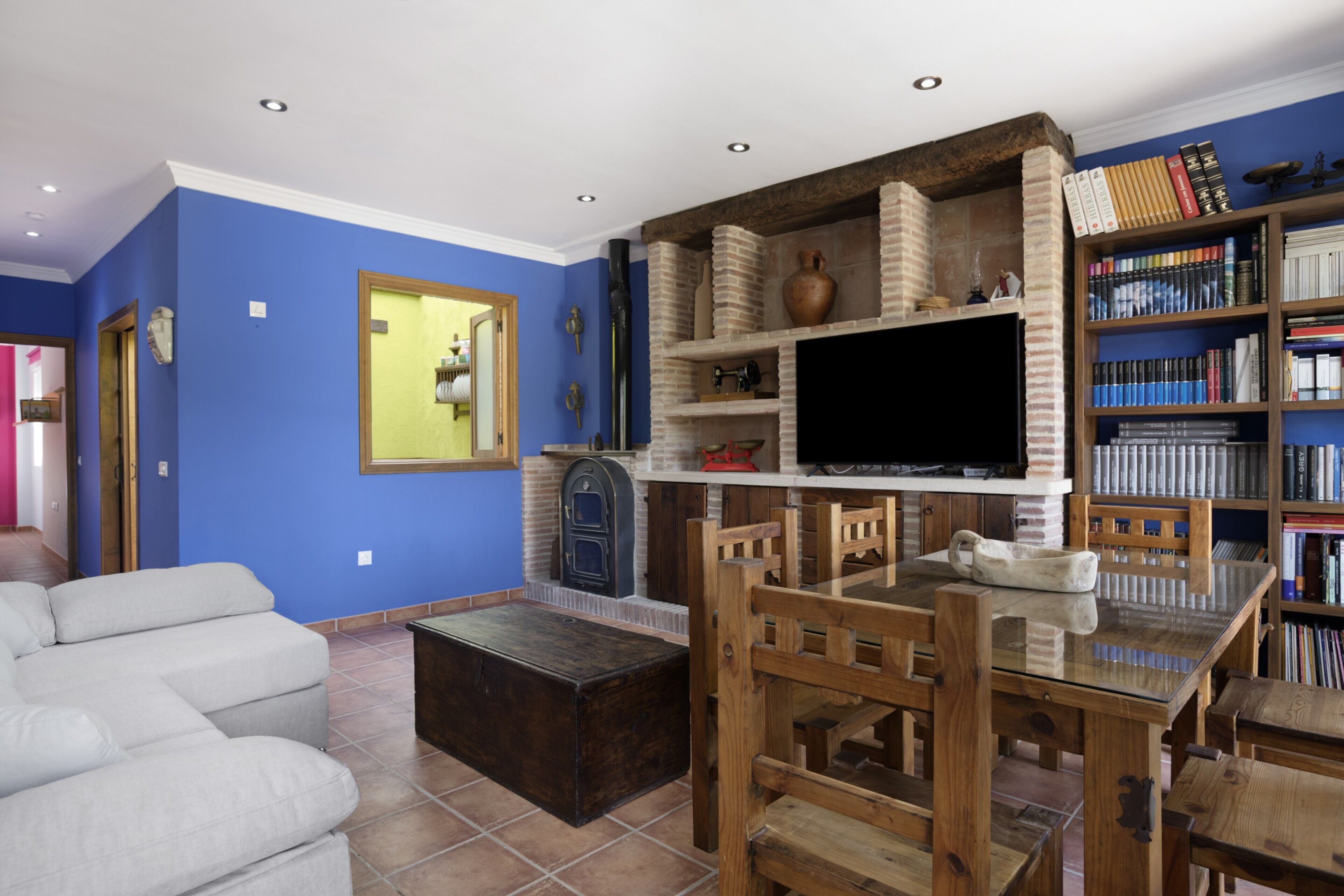A living room with a sofa, a wooden dining table, a TV, a fireplace, and a bookshelf.