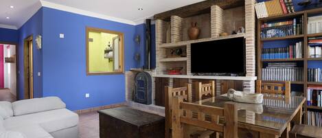 A living room with a sofa, a wooden dining table, a TV, a fireplace, and a bookshelf.