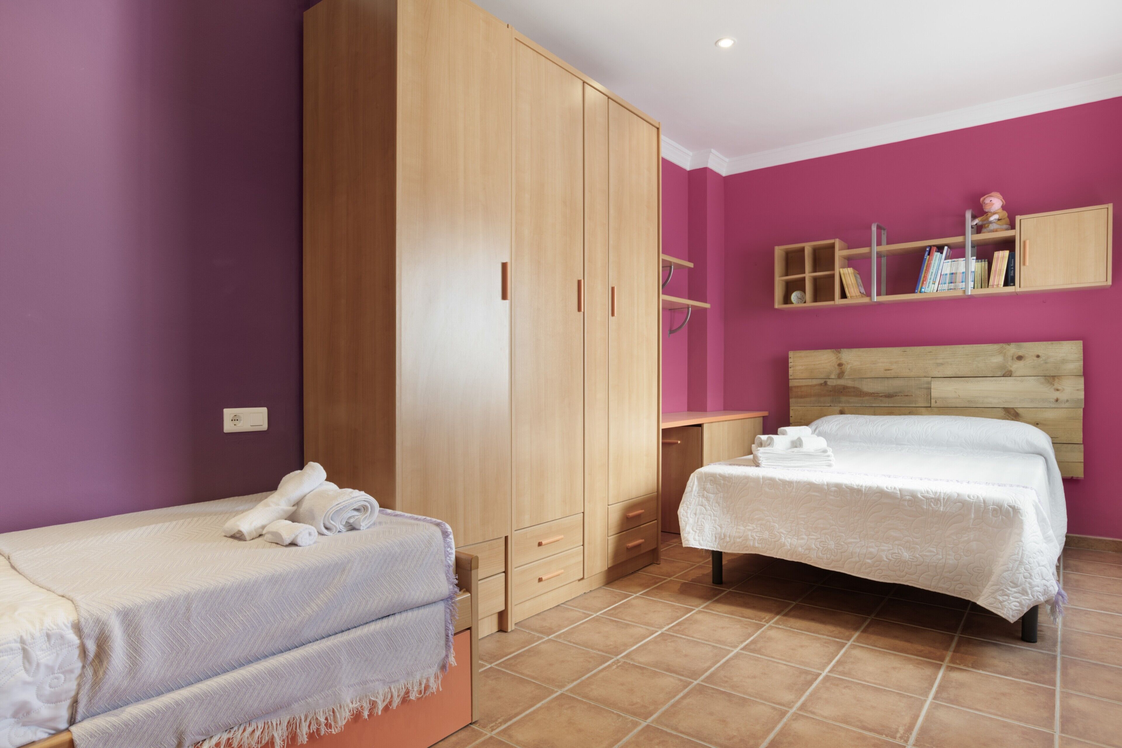 Un dormitorio con una cama, un armario, una mesita de noche y una estantería con libros.