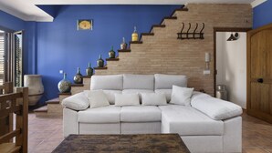 A living room with a sectional sofa, a coffee table, a staircase with decorative bottles, and a door with a coat rack. - Apartment 'Las Niñas' with Private Terrace, Wi-Fi and Air Conditioning (Olvera)