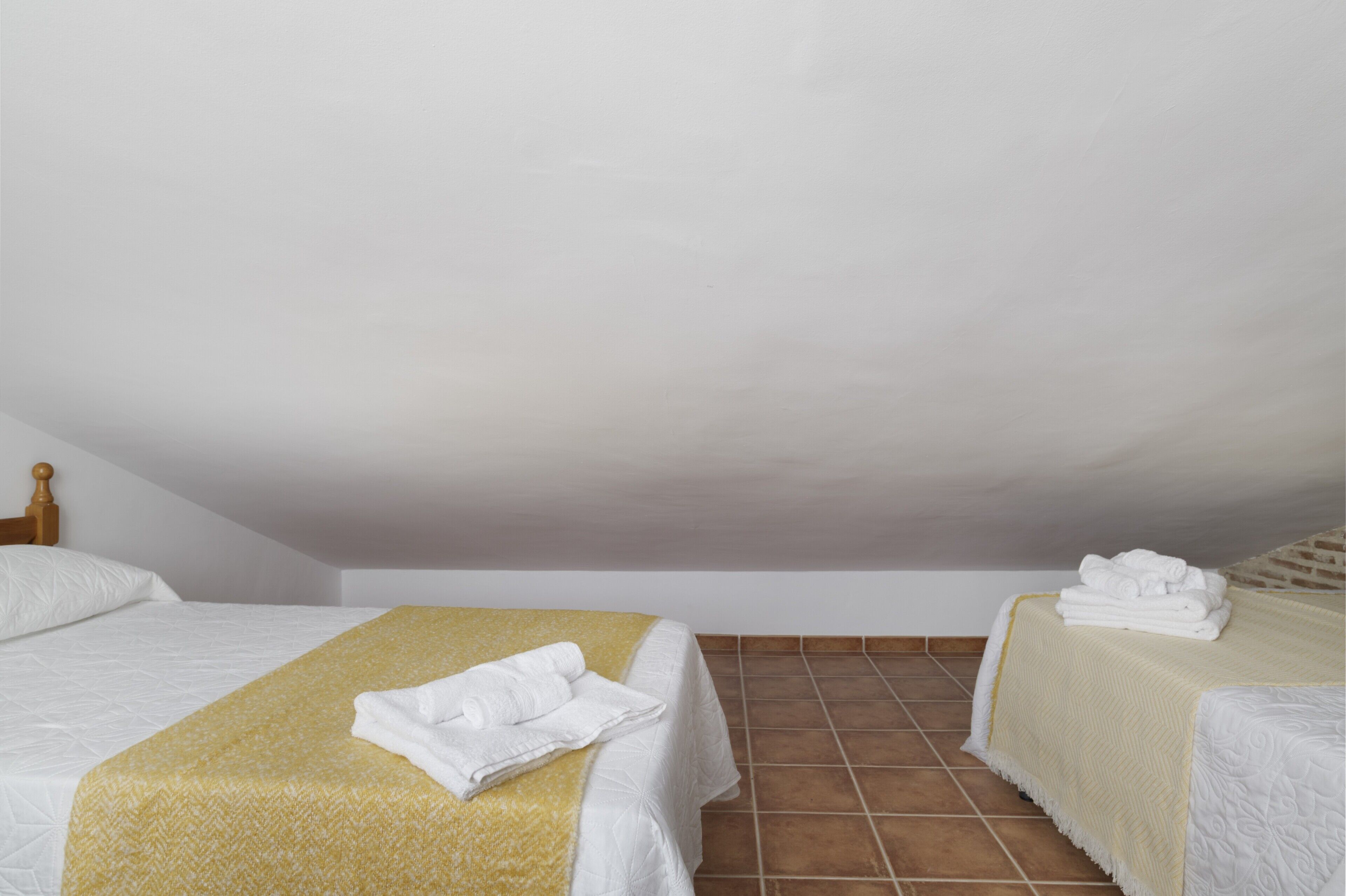 A room with two beds, each with a white bedspread and a yellow blanket.