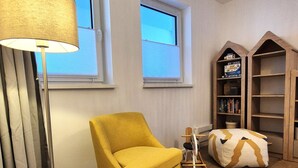 A cozy reading nook with a yellow armchair, a floor lamp, a patterned ottoman, and a wooden bookshelf. - Spacious Winterberg Stay for 7 Guests (Winterberg)
