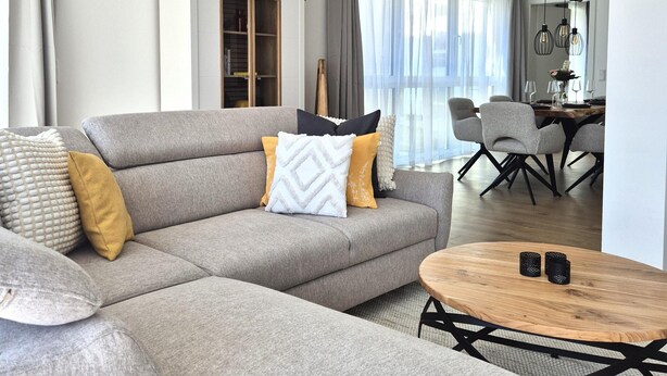 A modern living room with a grey sofa, a round wooden coffee table, and a dining area in the background. - Spacious Winterberg Stay for 7 Guests (Winterberg)