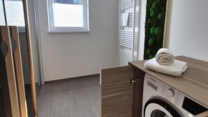 A compact laundry room with a built-in washing machine, a wooden cabinet, and a window with blinds. - Spacious Winterberg Stay for 7 Guests (Winterberg)