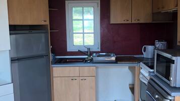 A compact kitchen with wooden cabinets, a refrigerator, a microwave, and a sink.