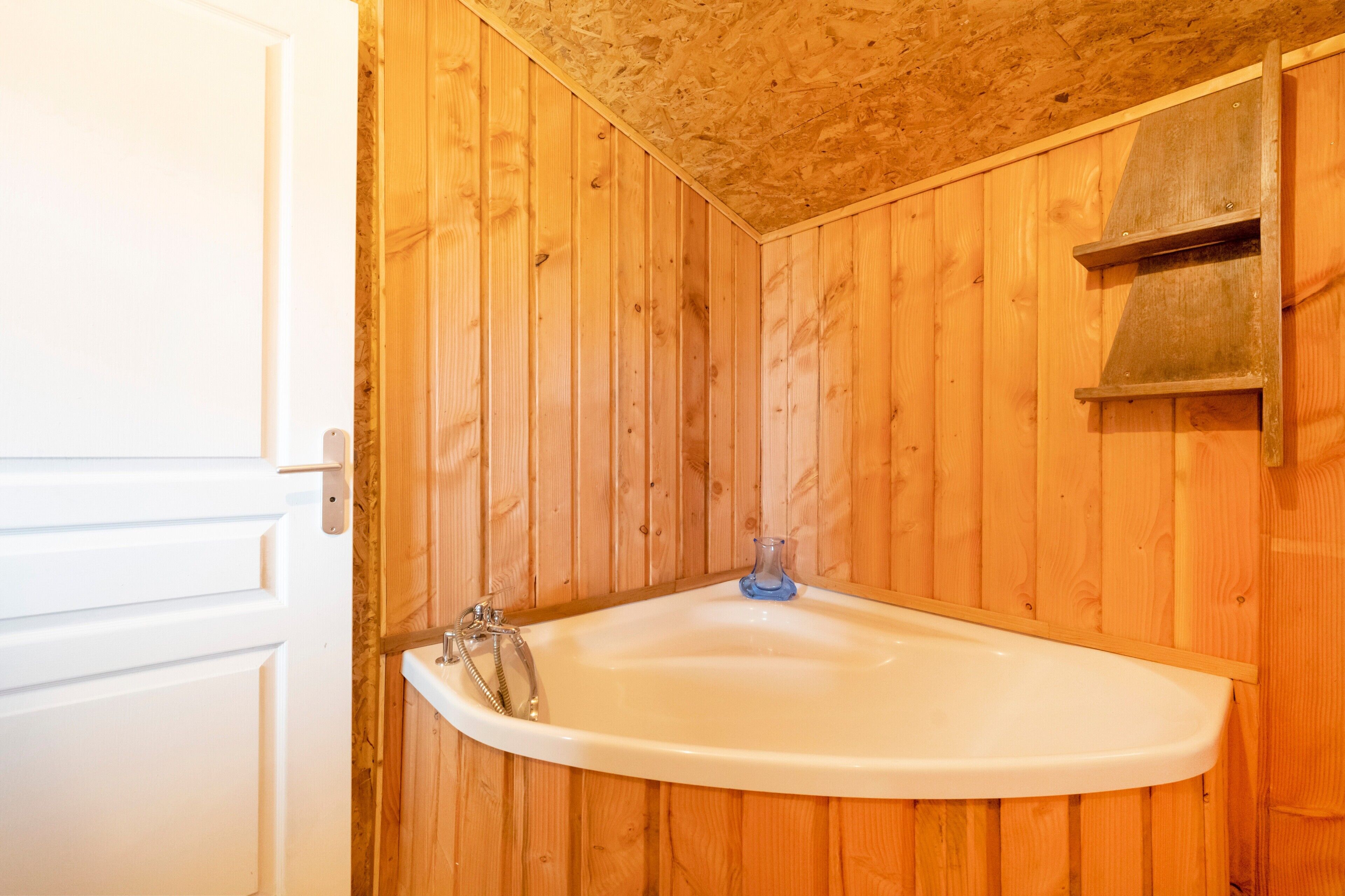 Une salle de bain avec des murs en bois, un lavabo blanc et une douche.