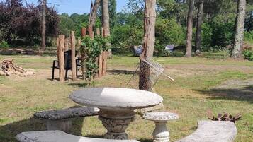 Taula i bancs de pedra a l'aire lliure en una zona enjardinada amb arbres al fons.