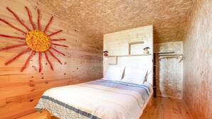 A wooden room with a bed, a sun decoration on the wall, and a shelf with items.