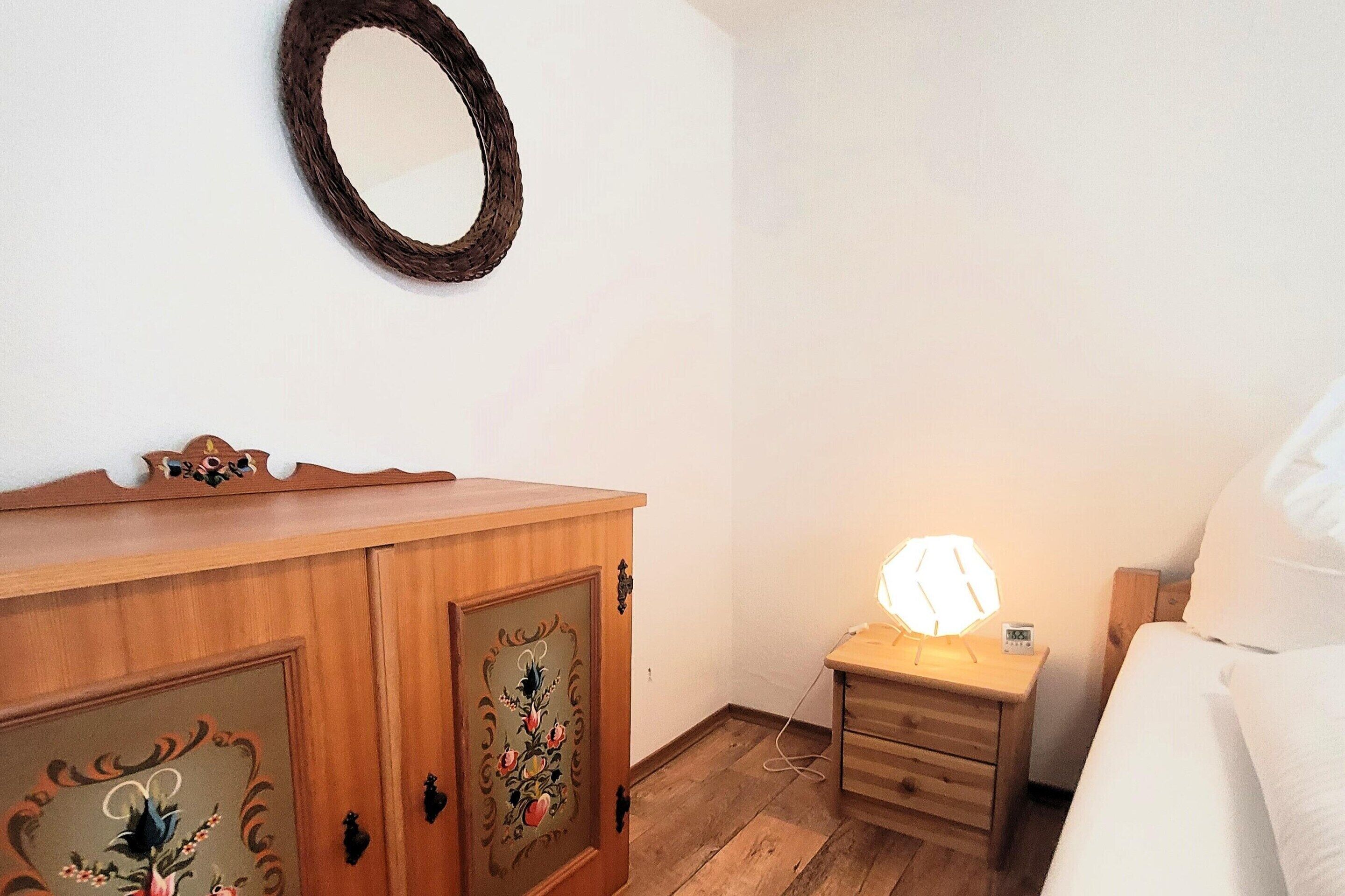 A bedroom with a wooden dresser, a bedside table with a lamp, and a bed.