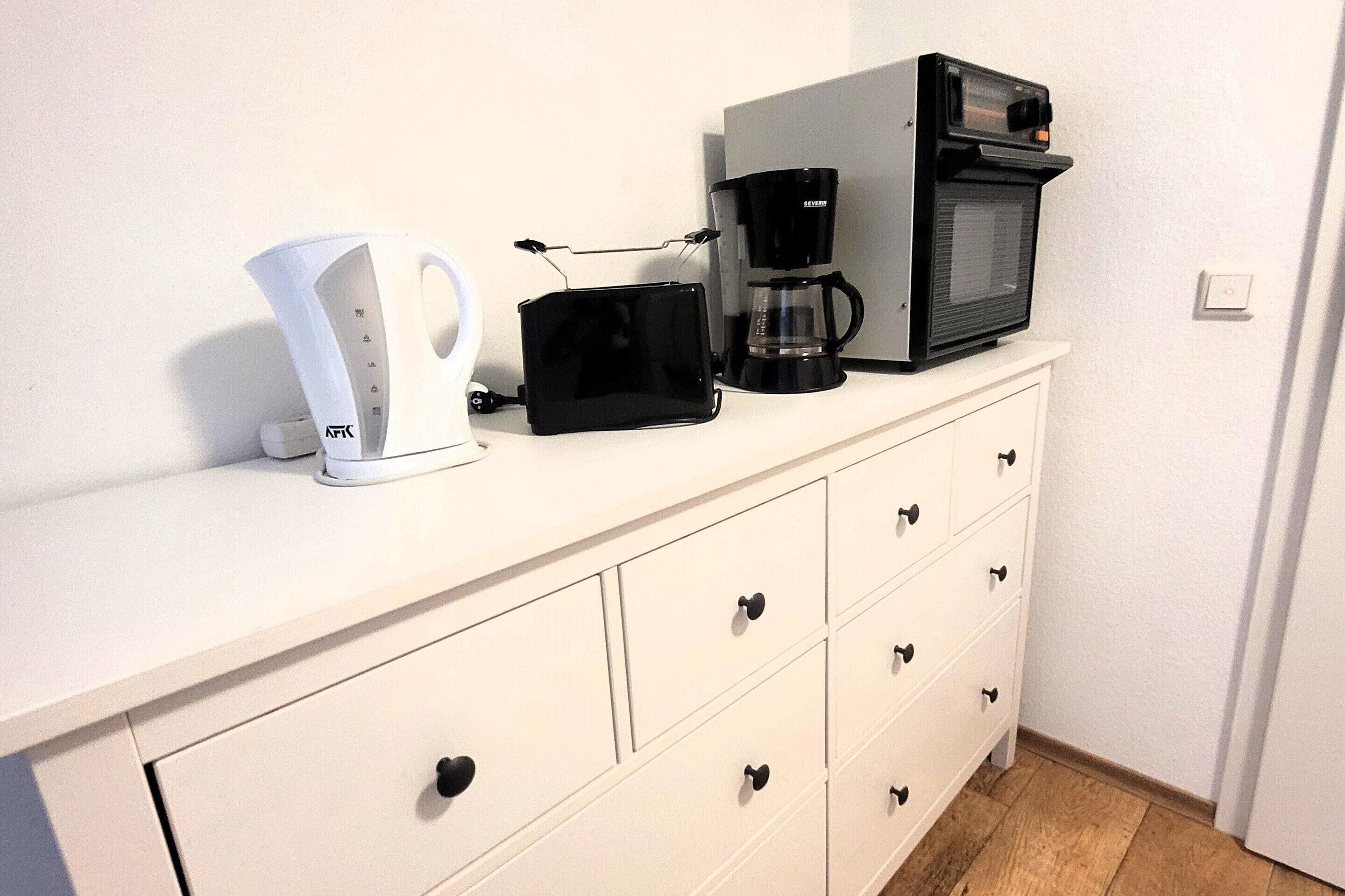 A kitchenette with a coffee maker, a toaster, and a microwave on a white cabinet.
