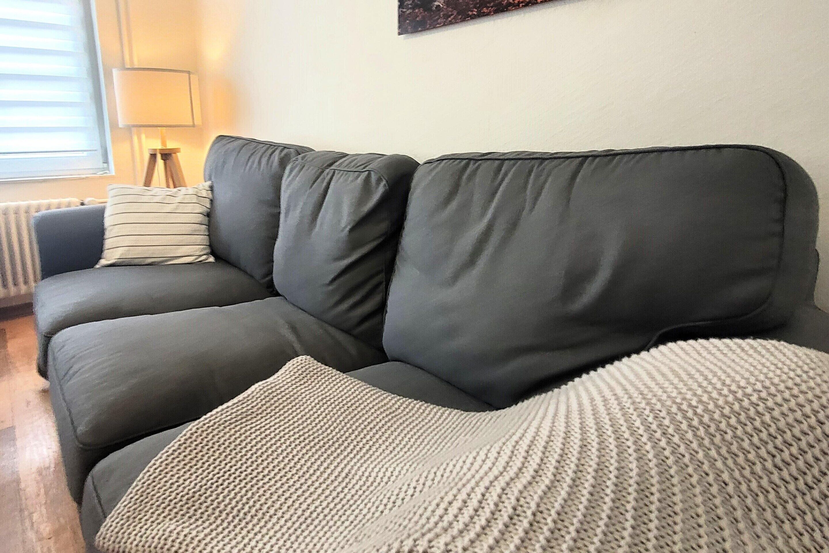 Un divano grigio con un cuscino a righe e una coperta lavorata a maglia.