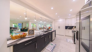 A modern kitchen with a large island, dark cabinets, and a stainless steel refrigerator.