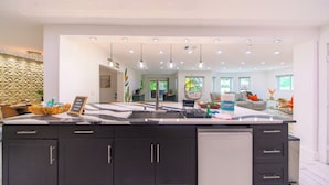 A modern kitchen with dark cabinets, a marble countertop, and pendant lighting.