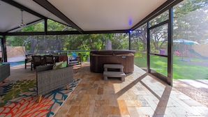 An outdoor patio with wicker furniture, a hot tub, and a view of a backyard.