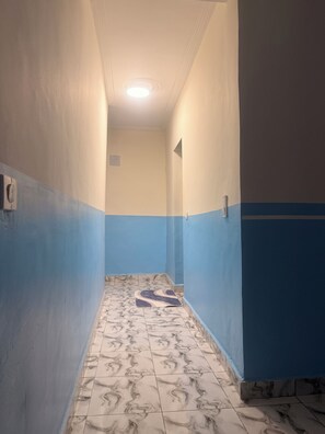 A narrow hallway with patterned floor tiles, walls painted in two-tone blue and beige, and a ceiling light.