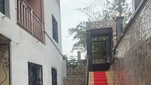A staircase with a red carpet leading to a gated entrance, surrounded by a stone wall with a tiled pattern. - Residence Yavanie Apartment with two bedrooms, two bathrooms, living room (Kribi)