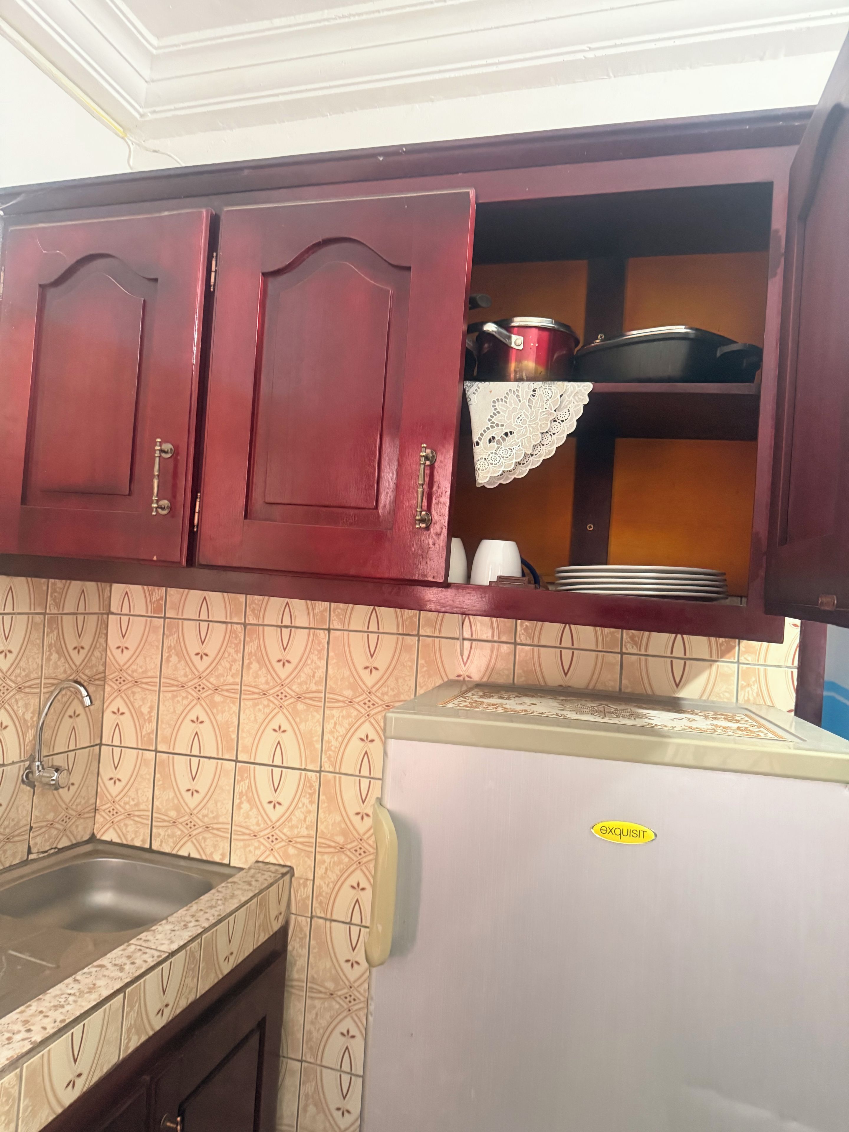 A kitchen with wooden cabinets, a tiled backsplash, a stainless steel sink, and a refrigerator with a sticker.