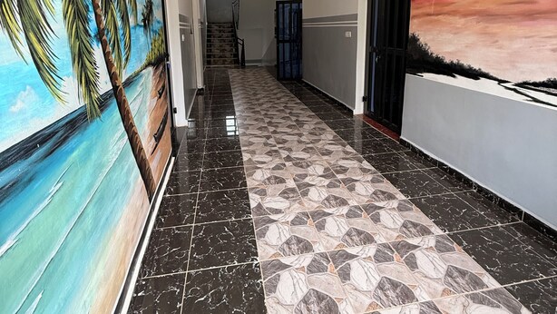A hallway with a tiled floor, a mural of a tropical scene on one wall, and a sunset mural on the opposite wall. - Residence Yavanie Apartment with two bedrooms, two bathrooms, living room (Kribi)
