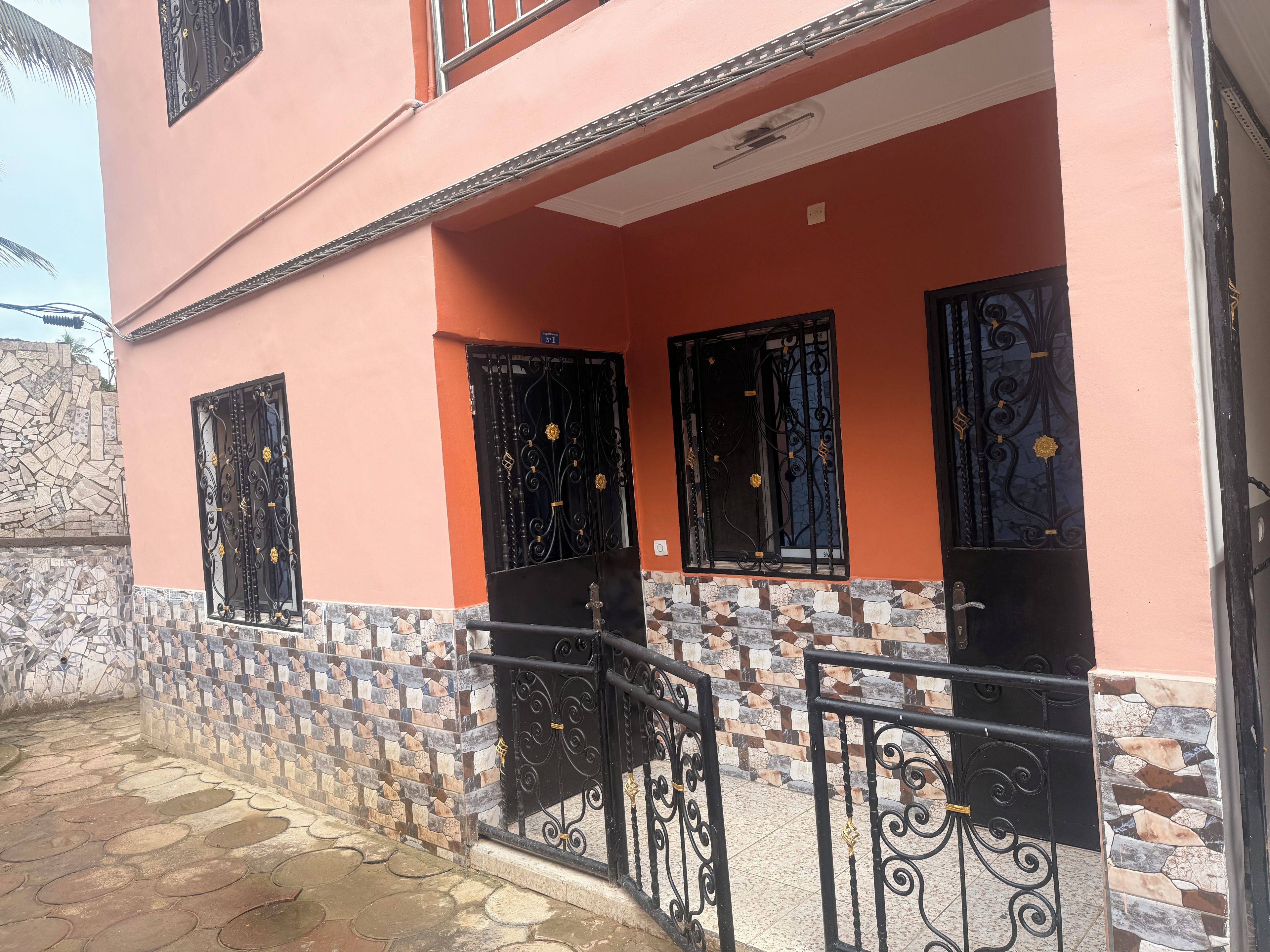 Un edificio de dos pisos con entrada de baldosas y rejas decorativas negras.