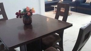 A dining area with a table and chairs, a vase of flowers, and a blue sofa in the background. - Residence Yavanie Apartment with two bedrooms, two bathrooms, living room (Kribi)