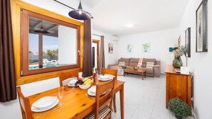 Un coin repas avec une table en bois dressée pour deux personnes, un canapé et une petite table d’appoint sur laquelle est posé un vase.