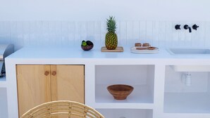 A modern kitchen with a white countertop, a wooden cabinet, a woven chair, and a bowl. - EBLI'7. HOTEL BOUTIQUE (Orihuela)