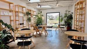 A modern cafe interior with wooden furniture, multiple tables, and shelves with items. - EBLI'7. HOTEL BOUTIQUE (Orihuela)