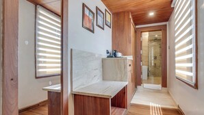 A hallway with wooden flooring, a marble bench, and a view into a bathroom with a shower. - Hotel Central Park (Srinagar)