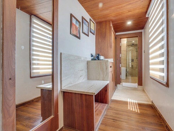 A hallway with wooden flooring, a marble bench, and a view into a bathroom with a shower. - Hotel Central Park (Srinagar)