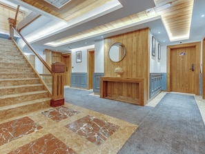 Un moderno vestíbulo de hotel con una escalera de mármol, mostrador de recepción de madera y un espejo grande.