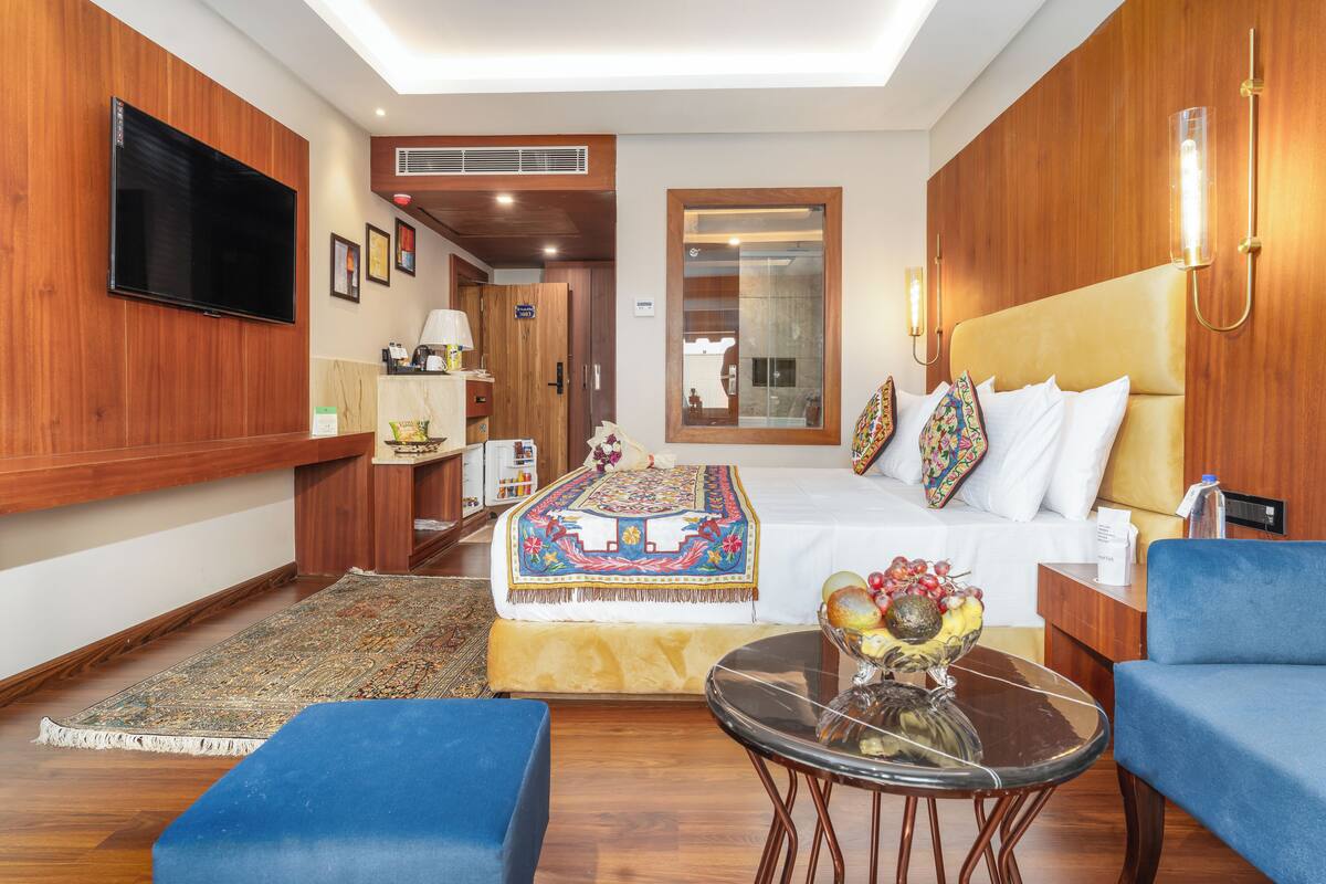 A modern hotel room with a large bed, a television, a desk, and a seating area.
