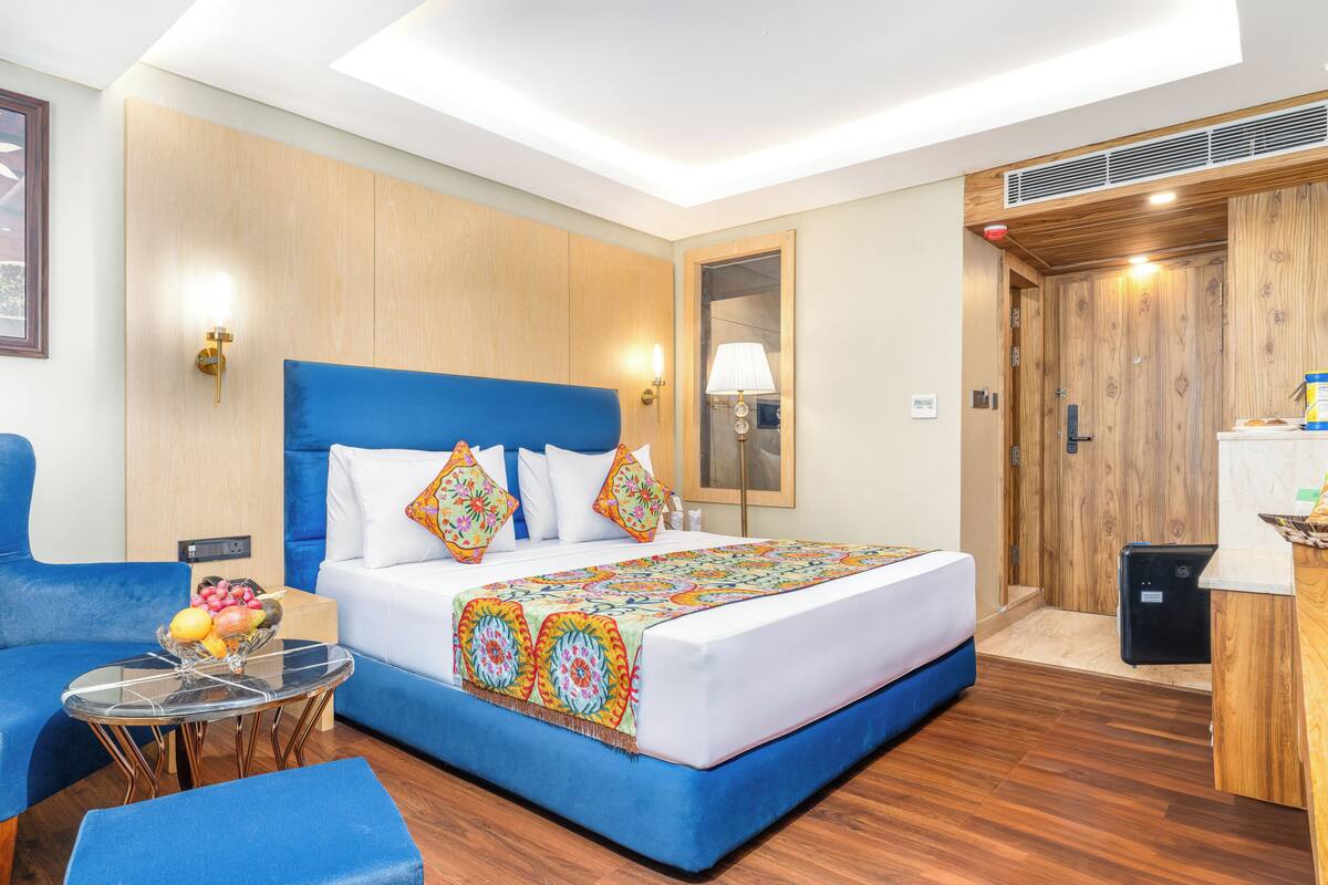 A hotel room with a large bed, a blue sofa, a small table with fruit, and a desk with a computer.