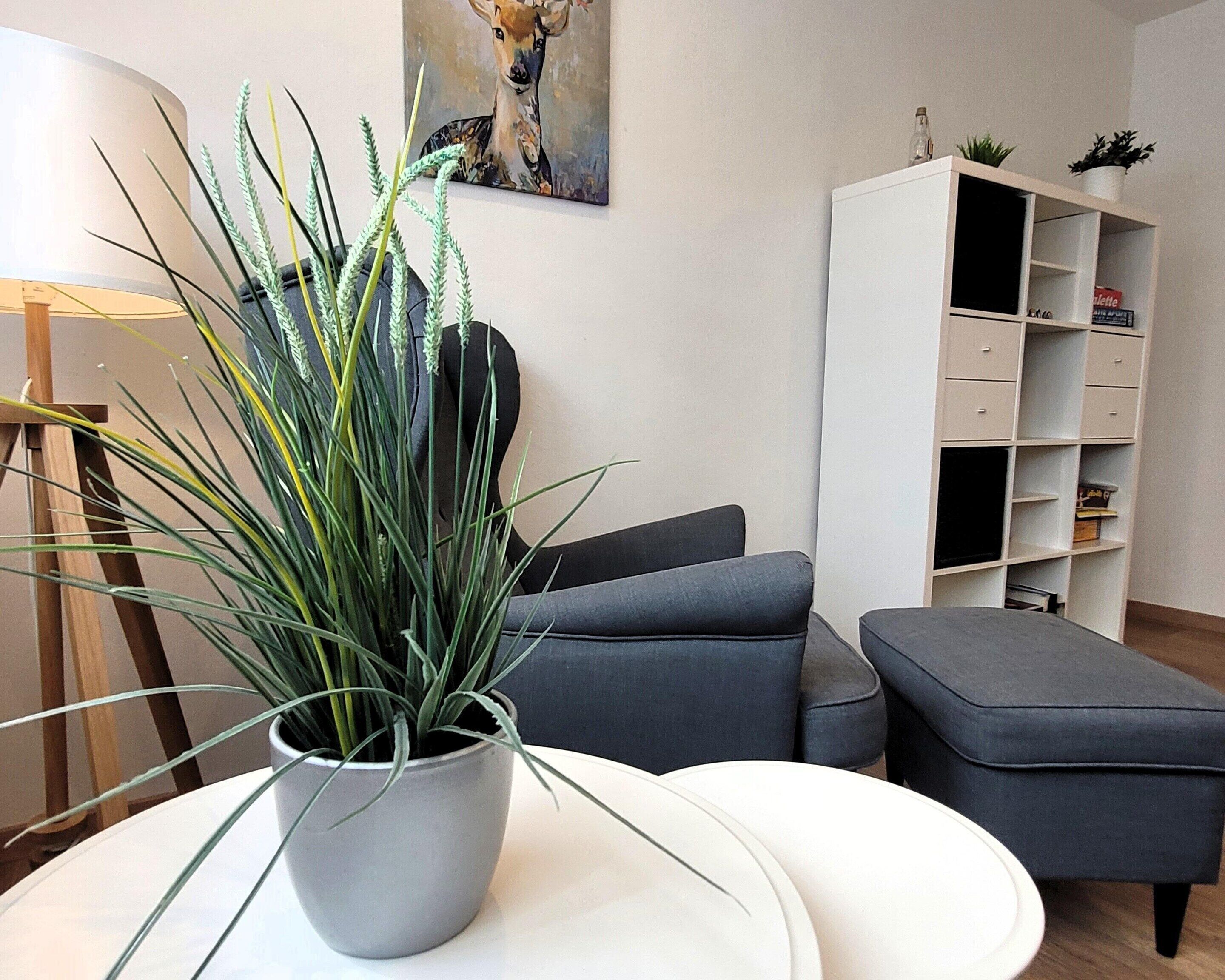 En moderne stue med en grå sofa, et hvidt bord og en potteplante.
