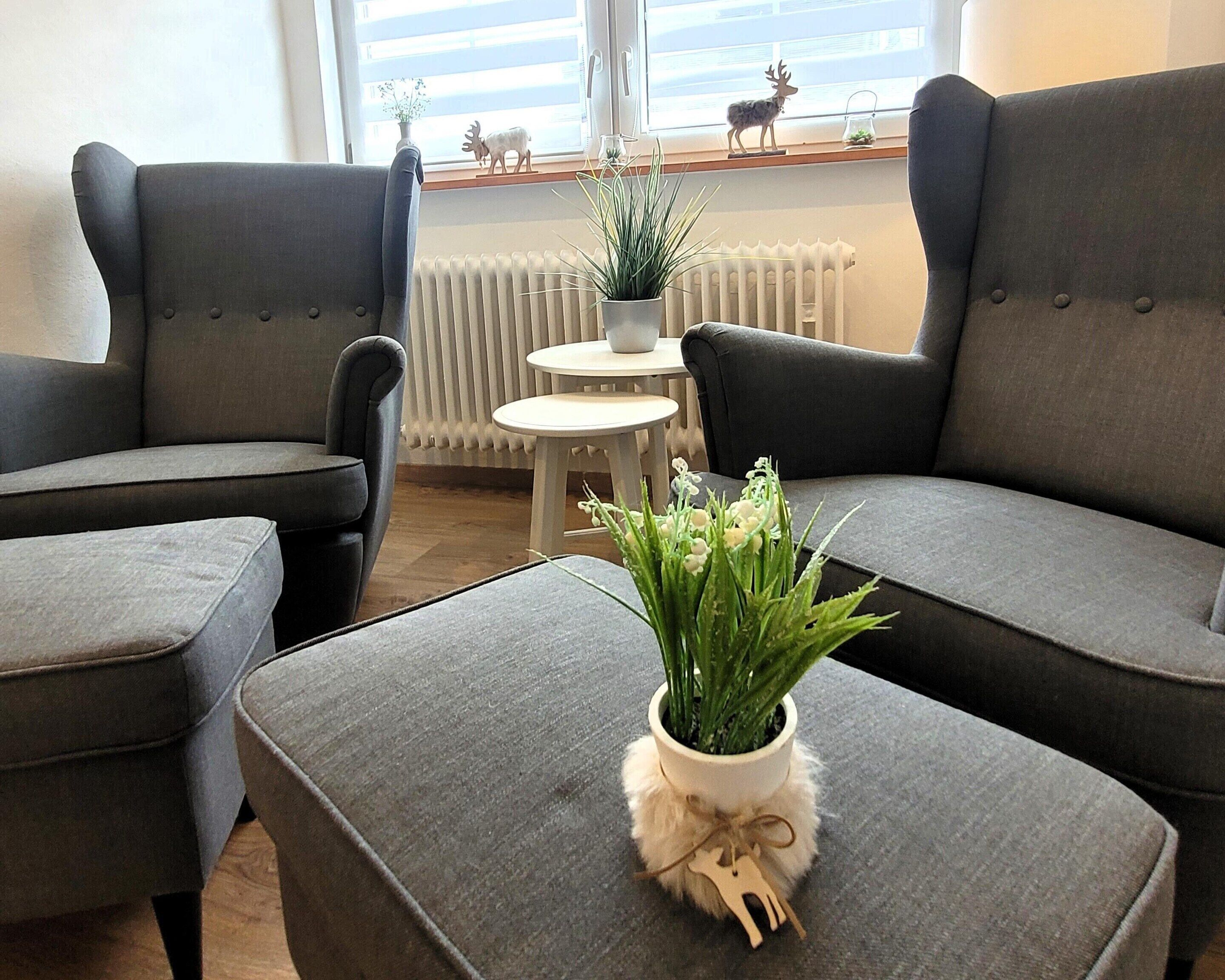 A modern living room with grey upholstered sofas, a small round table, and a potted plant on a matching ottoman.