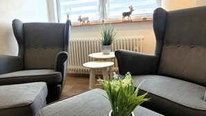 A modern living room with grey upholstered sofas, a small round table, and a potted plant on a matching ottoman. - Apartment in Winterberg Near Ski Lift (Winterberg)