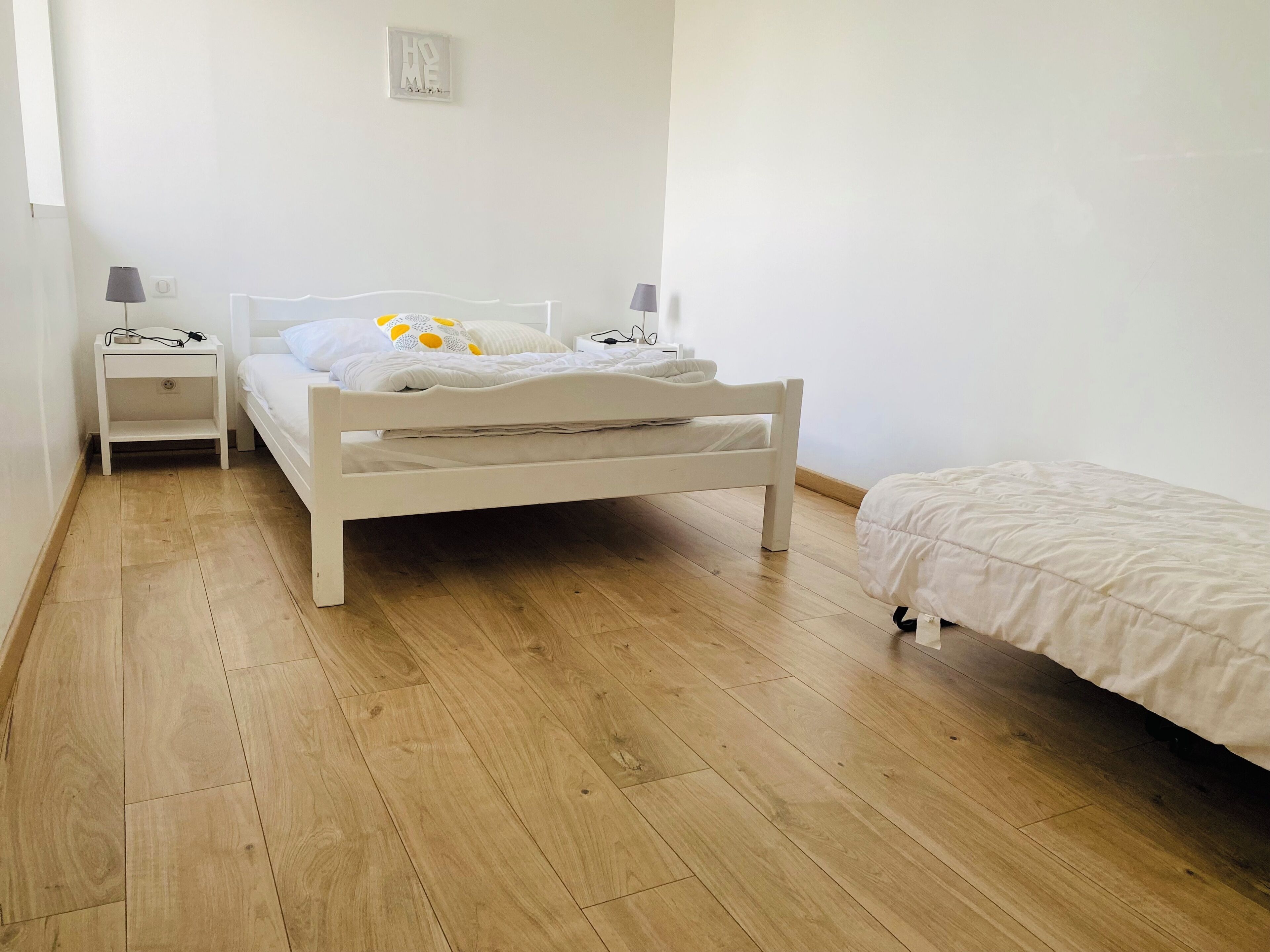Un dormitorio con una cama blanca, una mesita de noche con una lámpara y una pequeña nochecera.