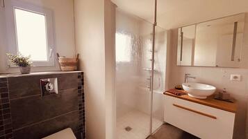 A bathroom with a glass shower enclosure, a white sink, and a toilet.
