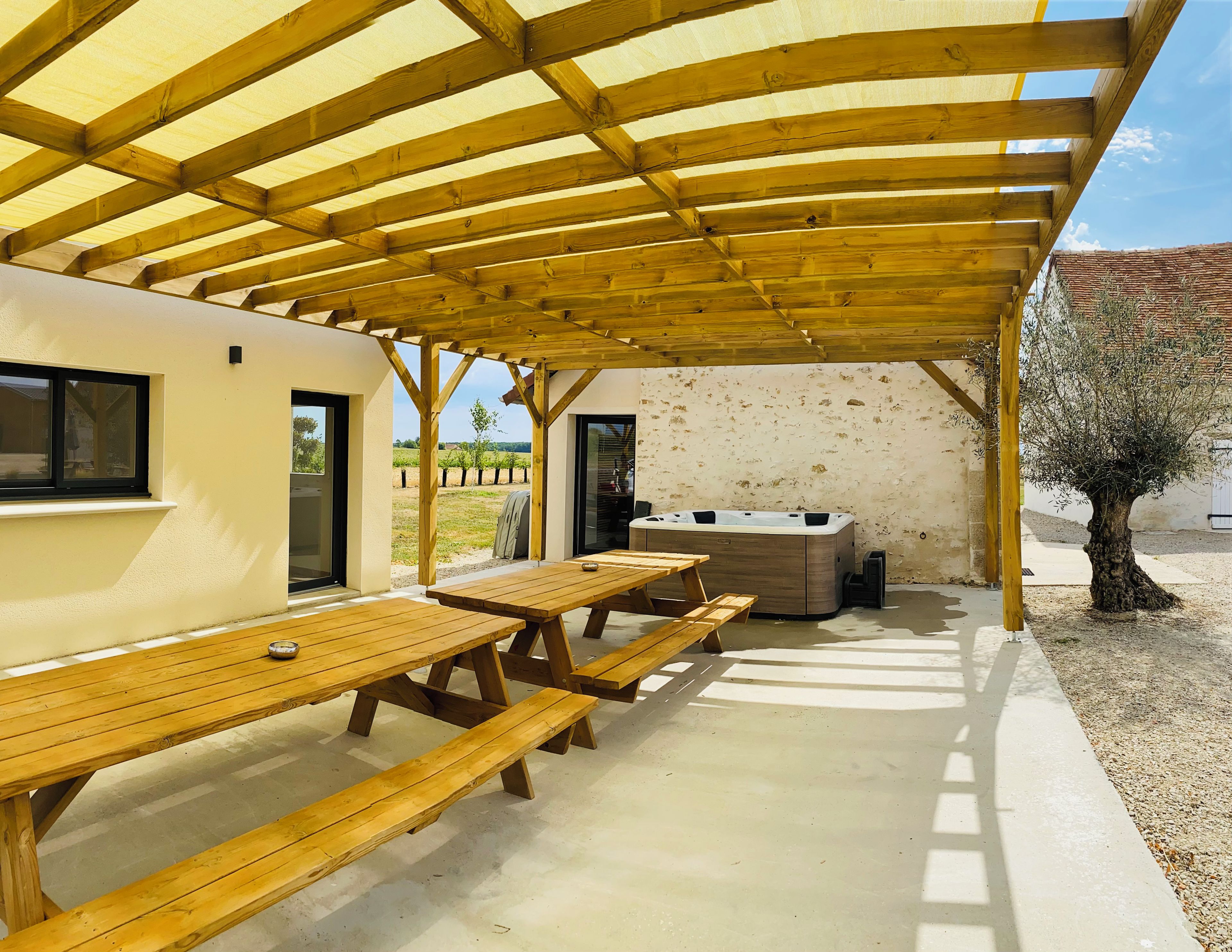 Una terrazza esterna con tavoli e panche in legno, una vasca idromassaggio e una pergola.