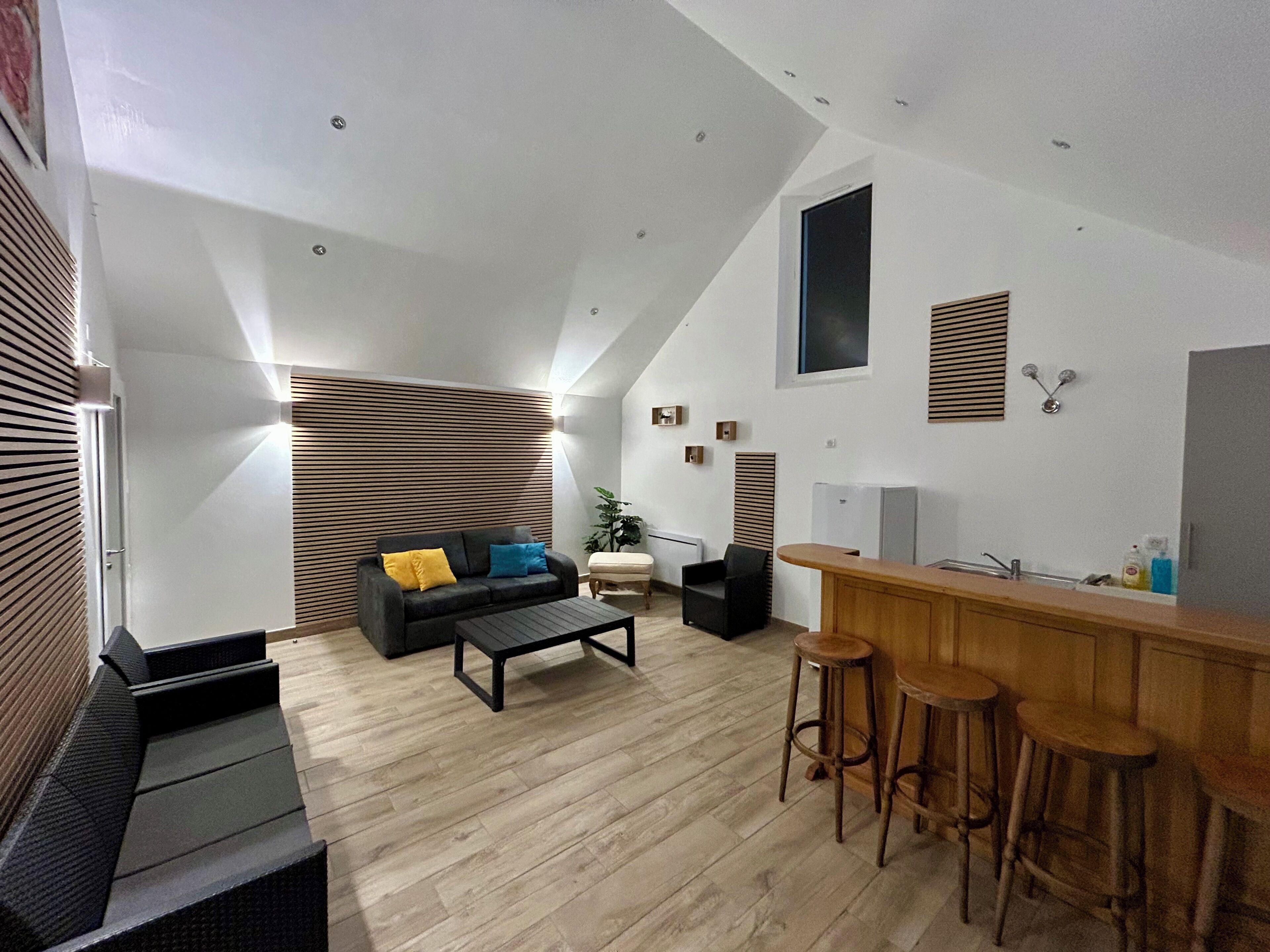 Una cocina moderna con encimera de madera y taburetes de bar, un sofá negro con cojines y una pared de listones de madera.