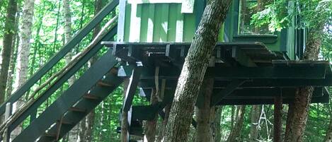 A treehouse with a green exterior, wooden stairs, and a platform area.