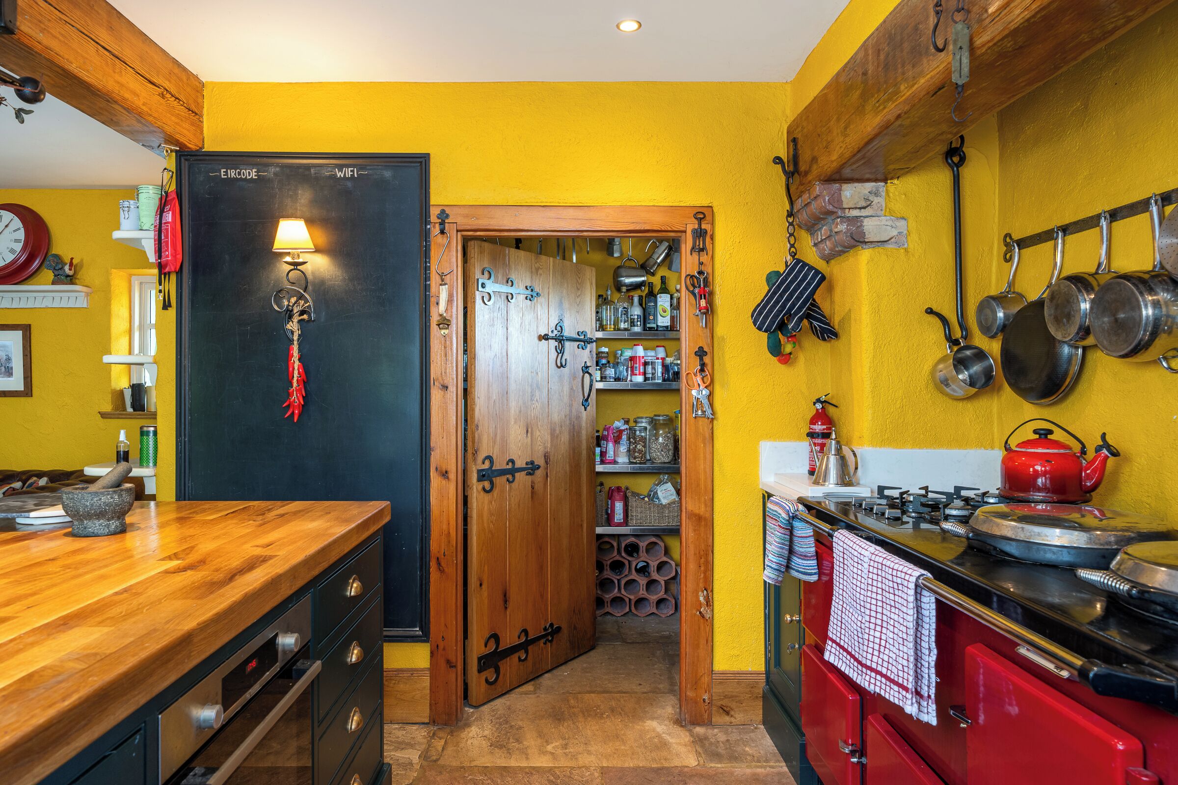 Een keuken met houten kastjes, een rode kookplaat en een gele wand.