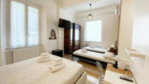 A hotel room with two beds, a desk with a computer, a TV, and a window with blinds. - Casa Granatelli (Palermo)