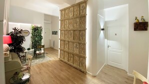 A spacious living room with a wooden floor, a large decorative panel, a dining area with a table and chairs, and a plant. - Casa Granatelli (Palermo)