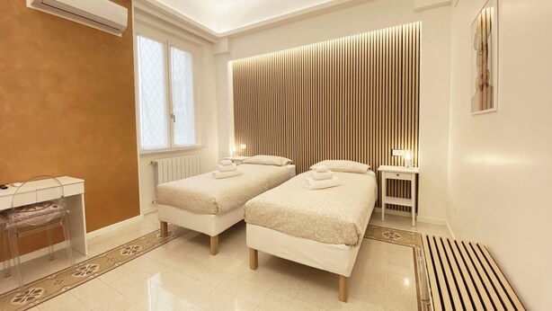 A modern hotel room with two beds, a radiator, a window, and a wall-mounted air conditioner. - Casa Granatelli (Palermo)