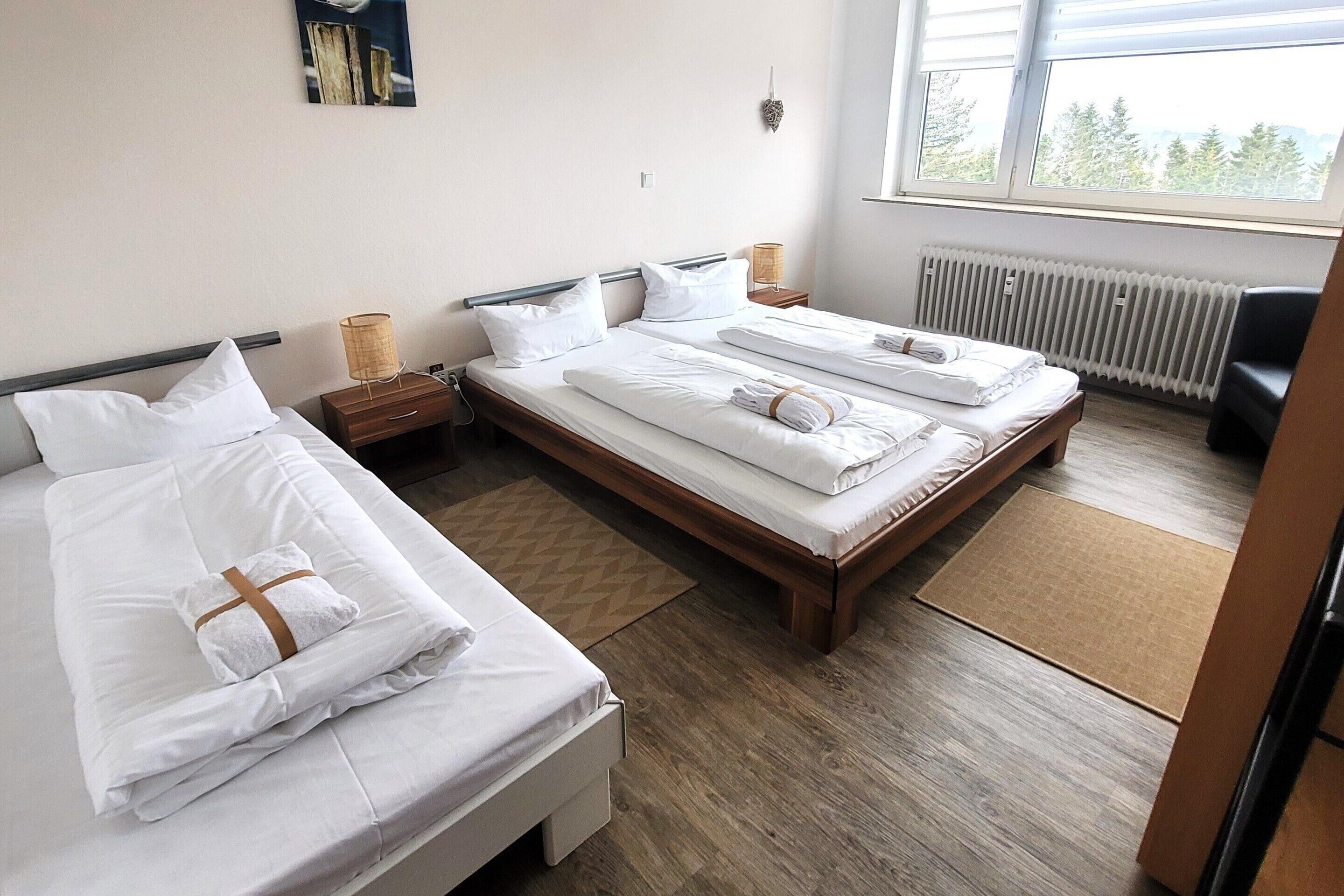 A hotel room with two beds, a wooden floor, a window with a view, and a radiator.