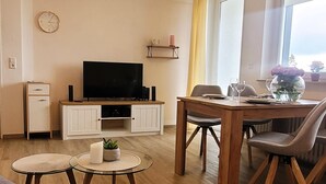 Un salon avec un téléviseur, une table à manger avec des chaises, une petite table basse et une plante en pot.
