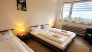 Une chambre d’hôtel avec deux lits simples, un plancher en bois, un radiateur et une fenêtre donnant sur des arbres.