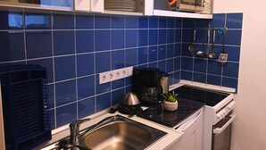 Une cuisine de taille réduite, avec des carreaux bleus, un évier en acier inoxydable, une machine à café et une cuisinière.