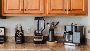 Een keuken met houten kastjes, een blender, een koffiezetapparaat en een messenblok.