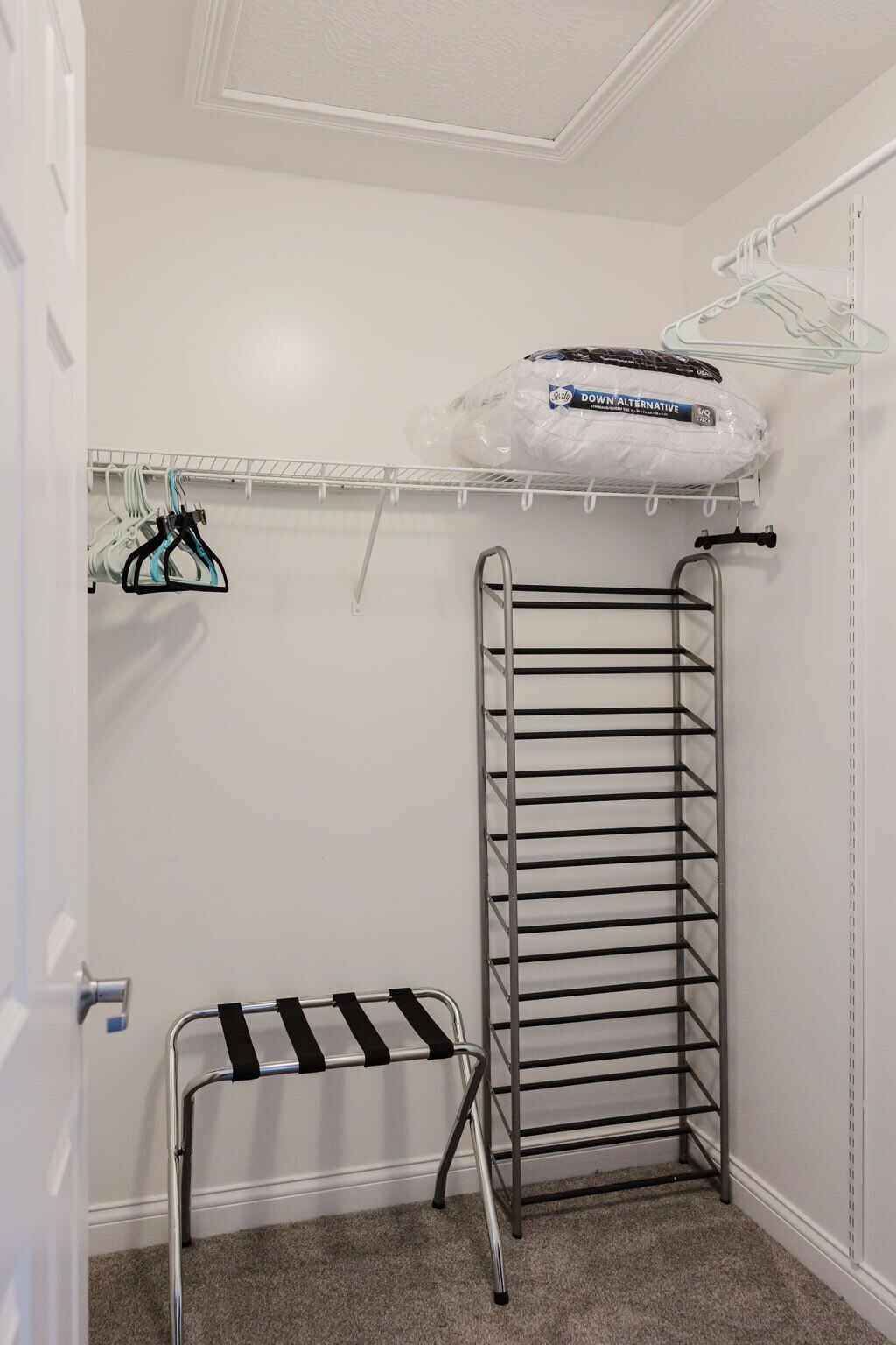A closet with a metal drying rack, a metal shelf with hanging clothes, and a plastic bag labeled "Down Alternative."